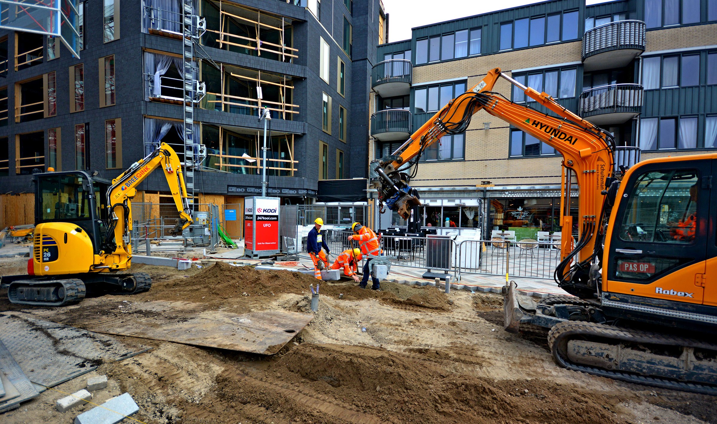 Kooi surveillance system monitoring an urban construction site with excavators and workers, ensuring security and safety during complex building operations in a residential area.
