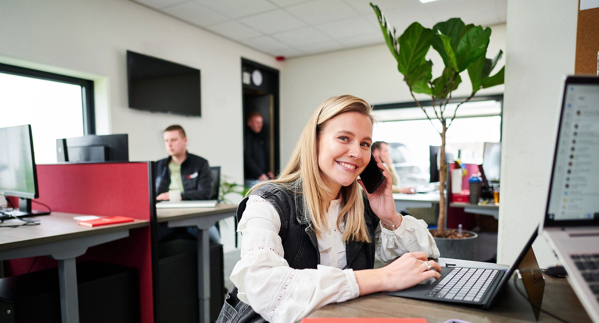 Kooi employee working in a modern office environment, multitasking on a laptop and phone, representing a reliable, innovative, and people-focused approach.