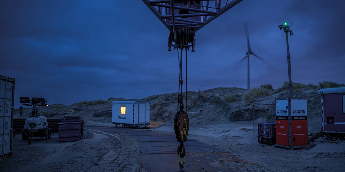 Kooi security units monitoring a construction site at night, with a wind turbine and equipment in the background, emphasizing a reliable, innovative, and robust approach to site safety and security.