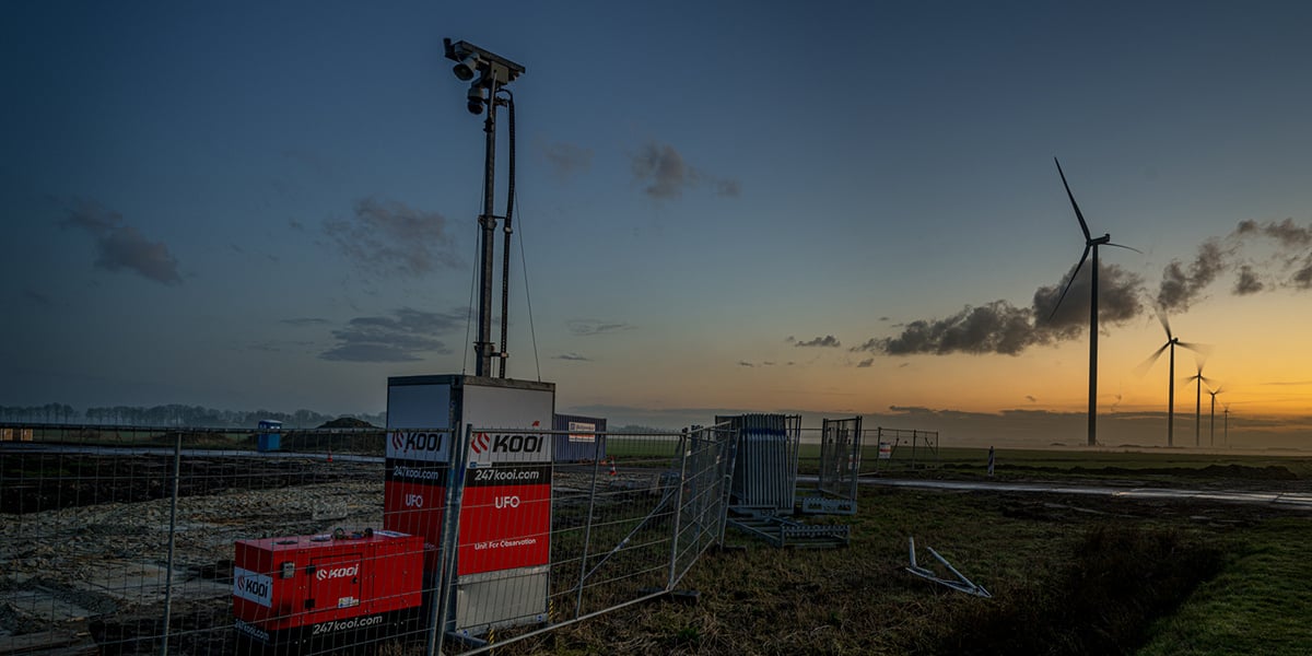 Kooi UFO security unit safeguarding a construction site at sunset, with wind turbines in the background, showcasing a reliable, innovative, and sustainable approach to site monitoring