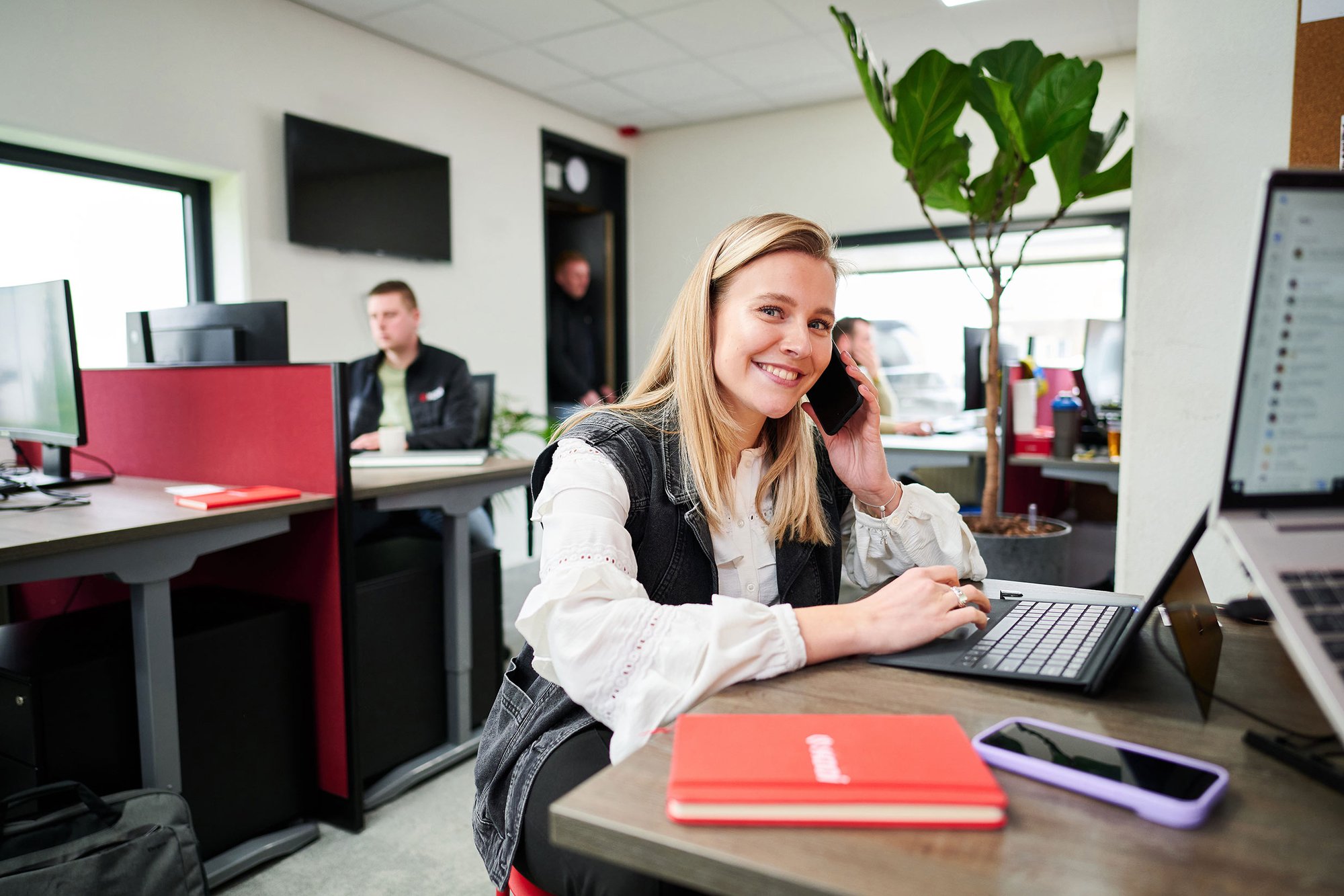 Kooi employee working in a modern office environment, multitasking on a laptop and phone, representing a reliable, innovative, and people-focused approach.