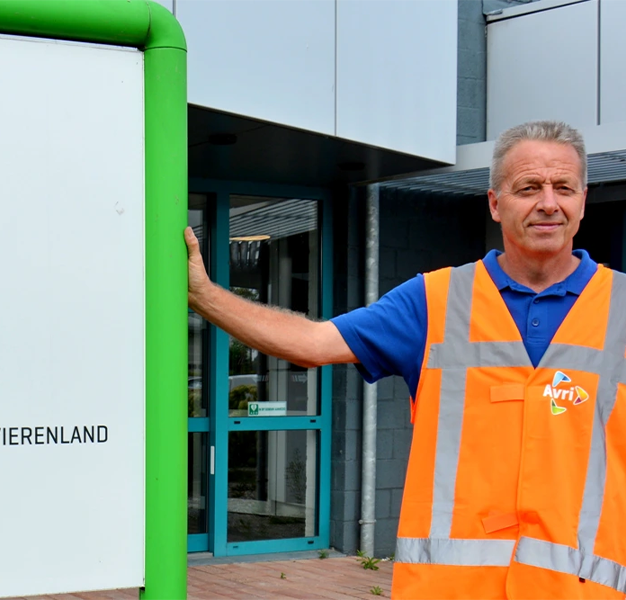 Gebouwbeheerder staat bij een bord en lacht