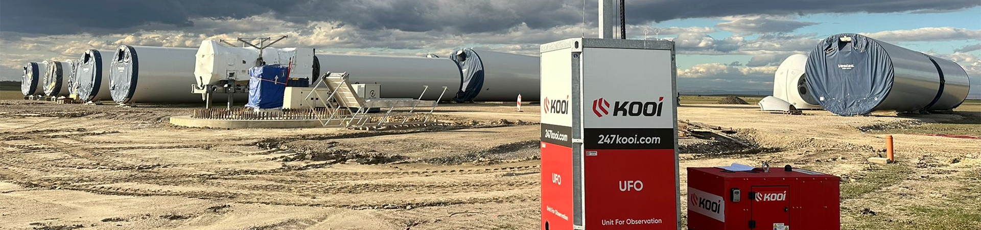 O unitate mobilă de securitate Kooi amplasată pe un șantier eolian, cu segmente de turbine eoliene depozitate în fundal pe un teren deschis.